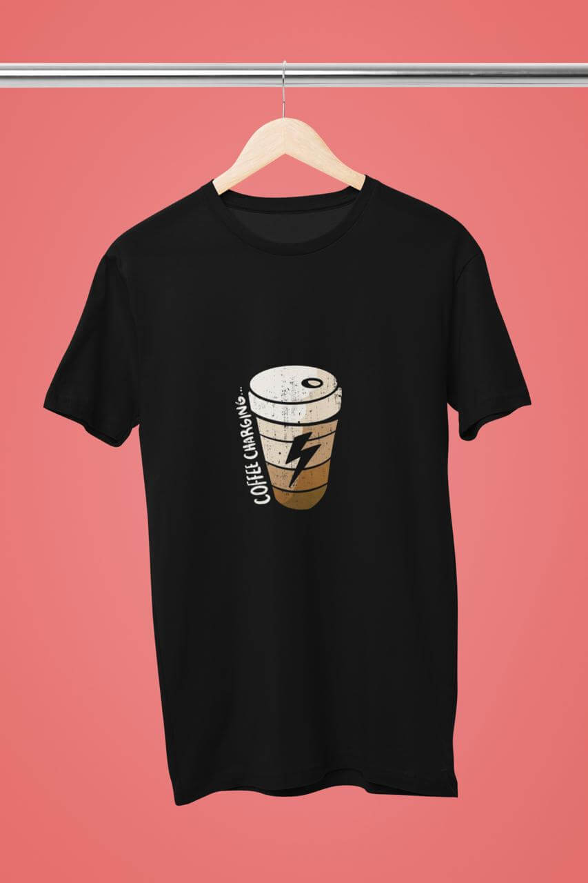 Unisex Coffee Charging Round Neck T-Shirt in black hanging on a wooden hanger against a pink background