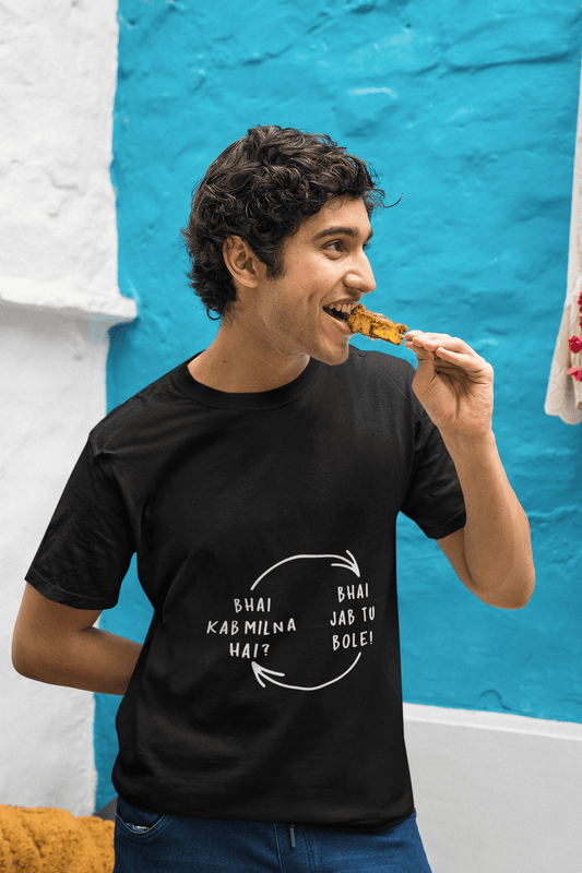 Man wearing a black funky round neck tee with "BHAI KAB MILNA HAI?" text, eating a snack against a blue and white background.