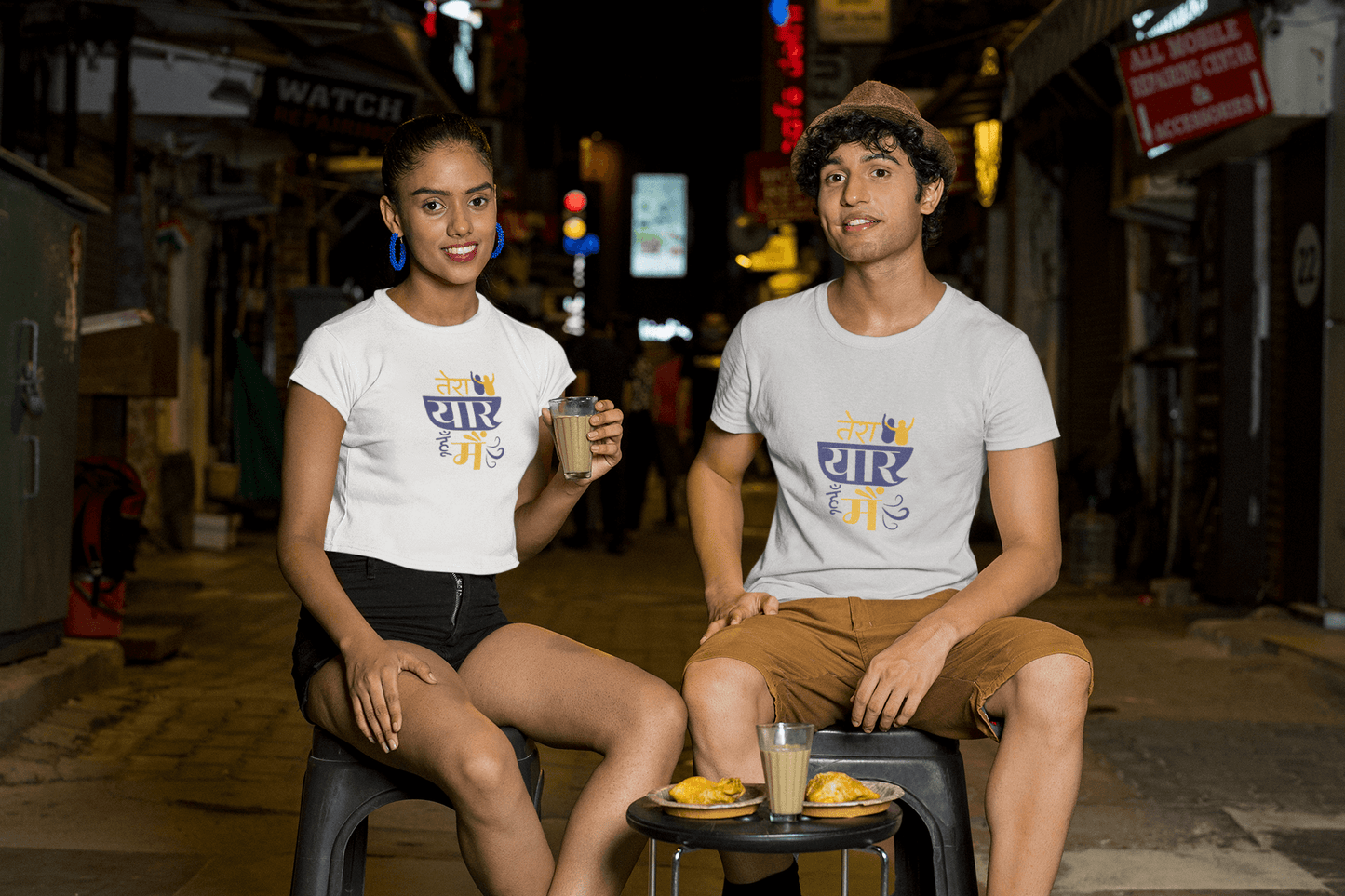 Two people wearing "TERA YAAR HOON MAIN" unisex T-shirts sitting and enjoying drinks outdoors