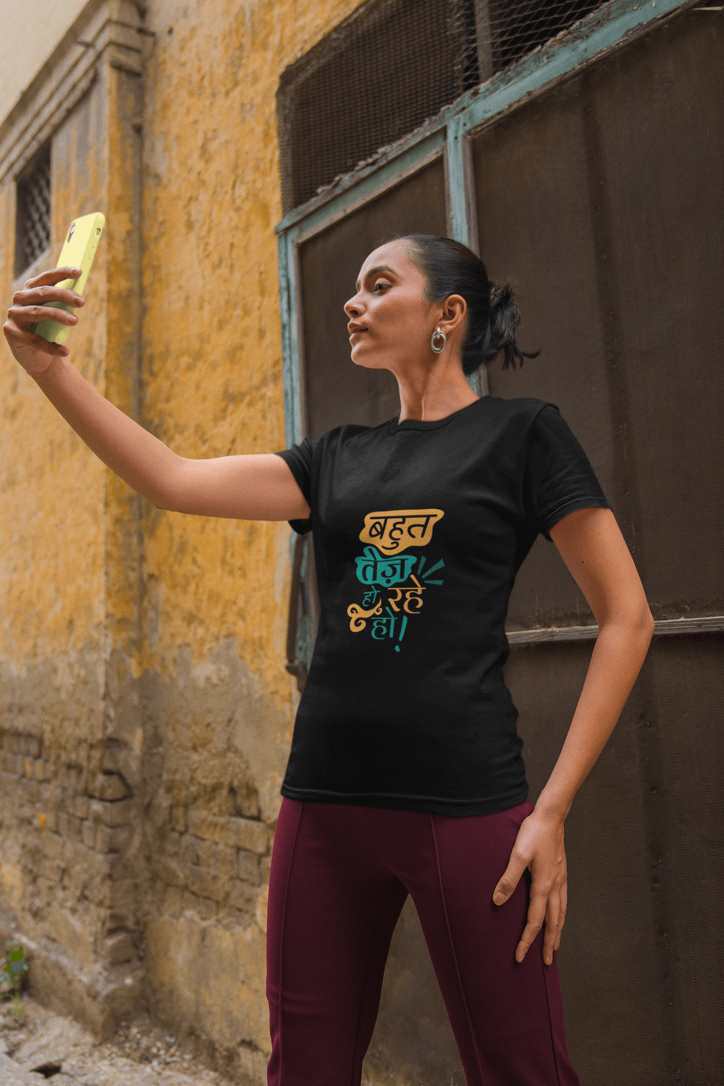 Woman taking selfie wearing black unisex T-shirt with "Bahut Tej Ho Rahe Ho" text in vibrant colors