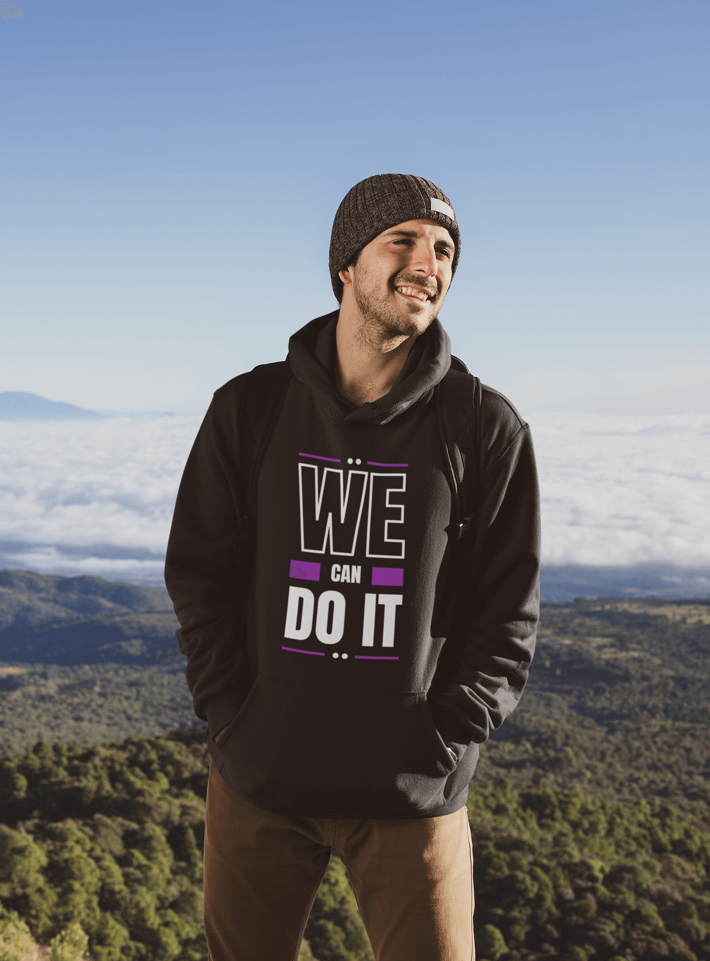 Young man wearing a "We Can Do It" hooded sweatshirt with a scenic mountain backdrop, showcasing style and warmth.