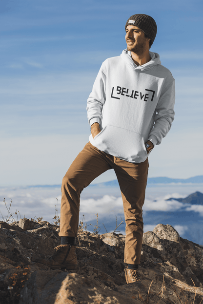 Man in a white Believe hooded sweatshirt standing on a rocky mountain top, showcasing a stylish winter look.