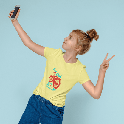 Girl wearing yellow "The Best Machine Ever Created" kids round neck t-shirt taking a selfie against a light blue background.